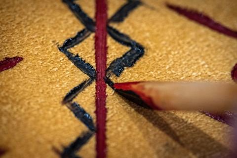 Person using wood styluses to apply paint and to scratch designs into the hides.